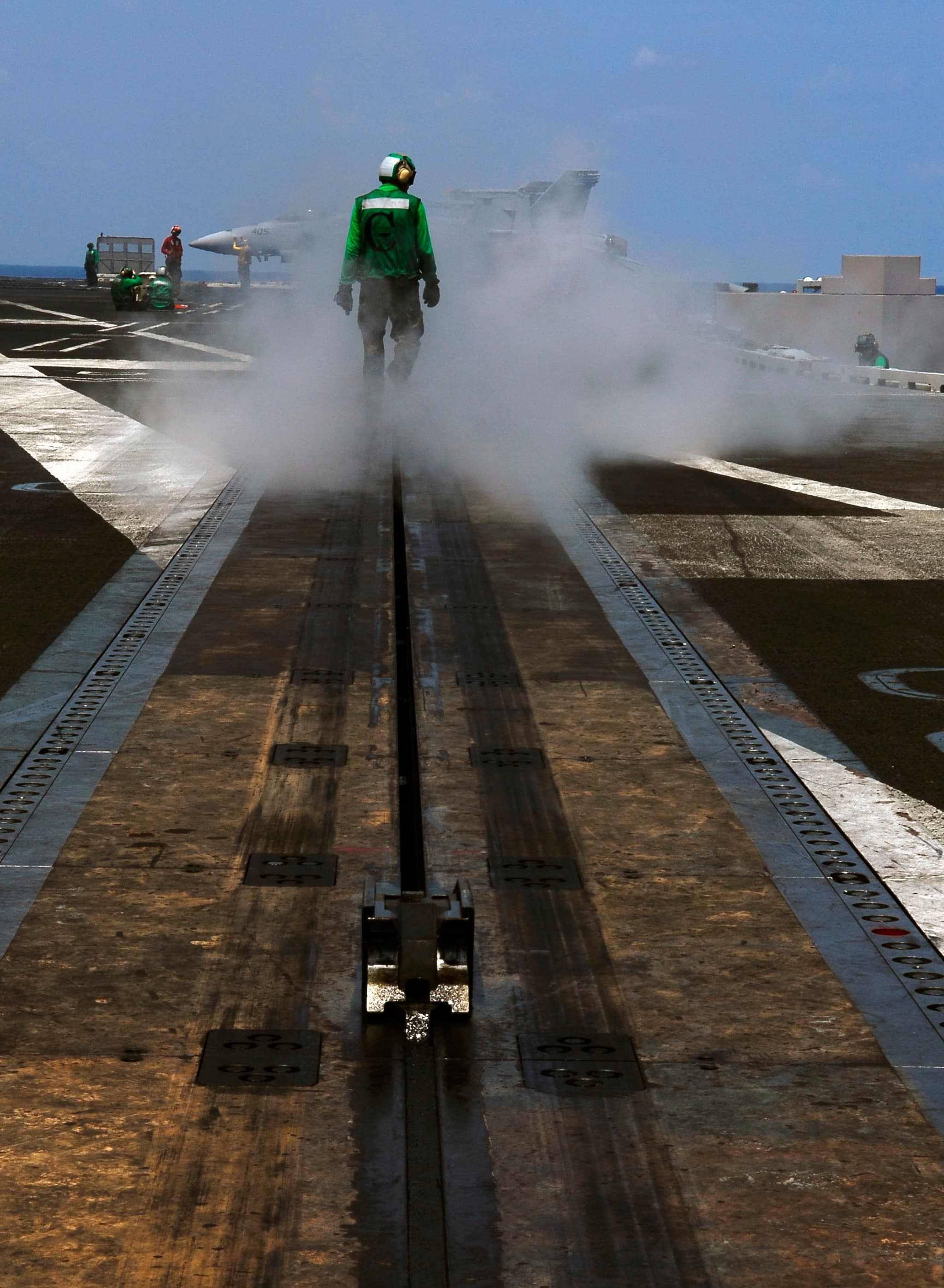 Fighter jet launching from an aircraft carrier catapult with steam visible on the flight deck