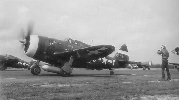 P-47 Thunderbolts with invasion stripes on an English airfield, propellers spinning before a mission