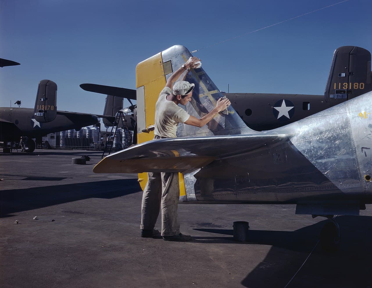 Worker painting the tail section of a P-51 Mustang on an outdoor assembly line