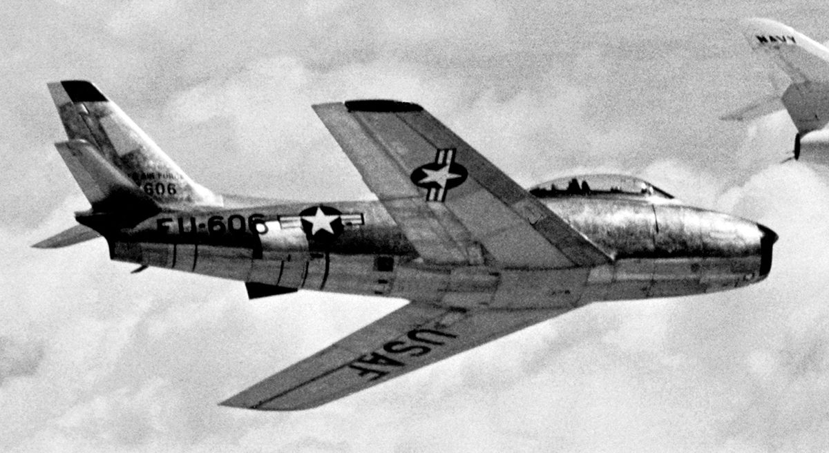 F-86 Sabre in bare metal USAF markings streaking across Korean skies