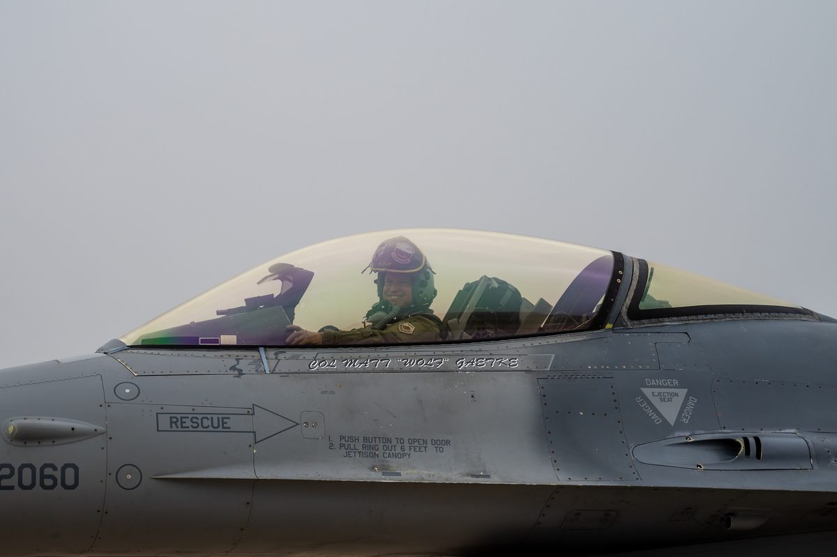 F-16 Fighting Falcon with heritage paint scheme flying over mountainous terrain in South Korea