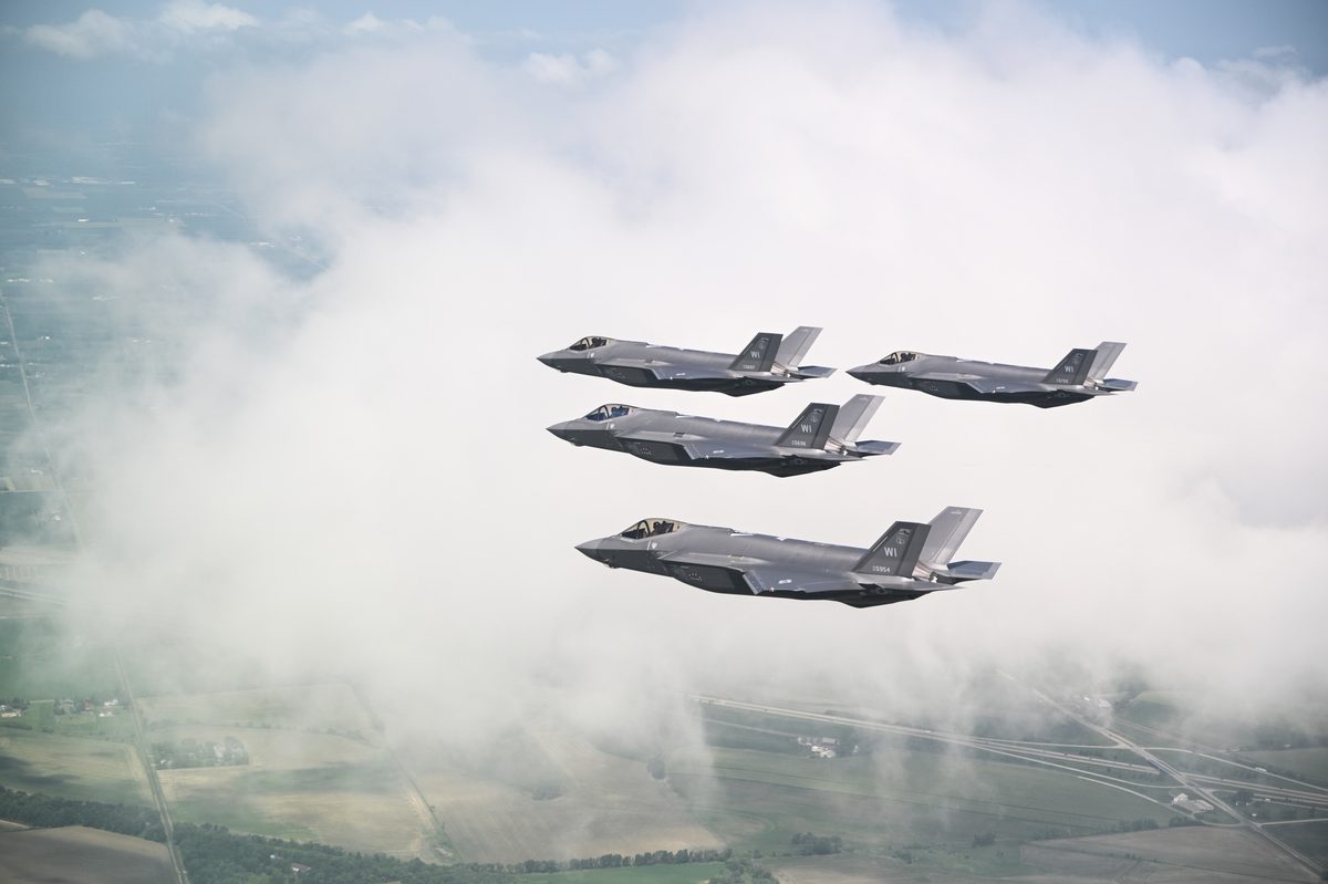 Multiple F-35 Lightning II aircraft flying in formation through clouds over rural Wisconsin during a training mission