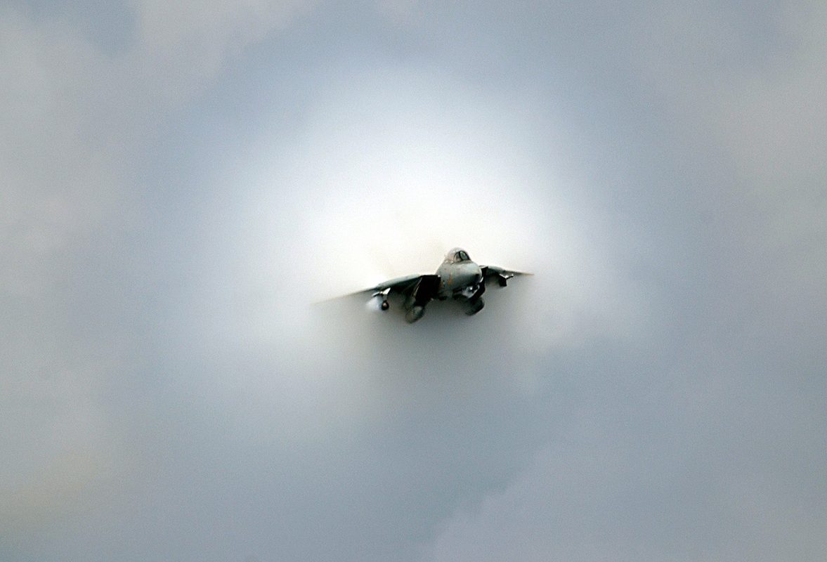 F-14 Tomcat at near-supersonic speed with vapor cone forming around the airframe