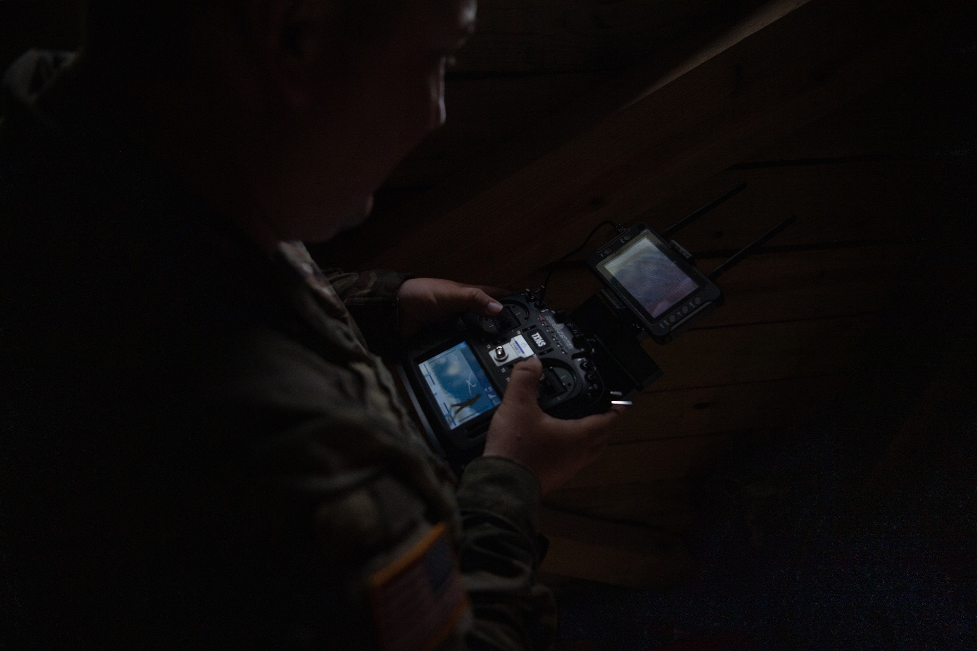 An FPV drone pilot wearing video goggles and holding a radio transmitter controller during flight operations