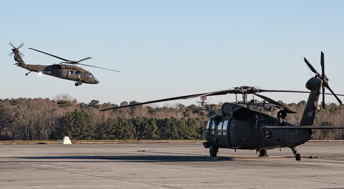 UH-60 Black Hawk helicopters at an airfield with one lifting off during operations