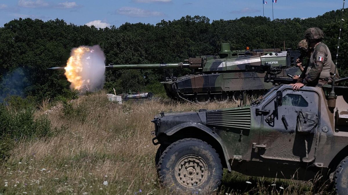 Leclerc tank firing its 120mm main gun during a live-fire exercise in a desert environment with muzzle flash visible