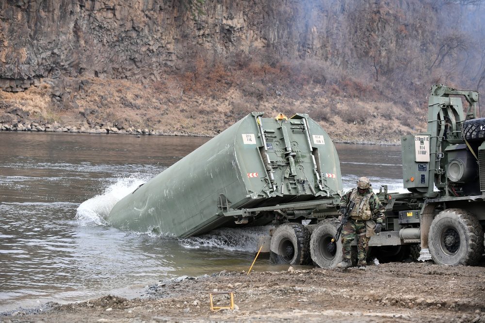 U.S. Army soldiers constructing a pontoon bridge section by section, with bridge boats maneuvering bay sections into position on the water